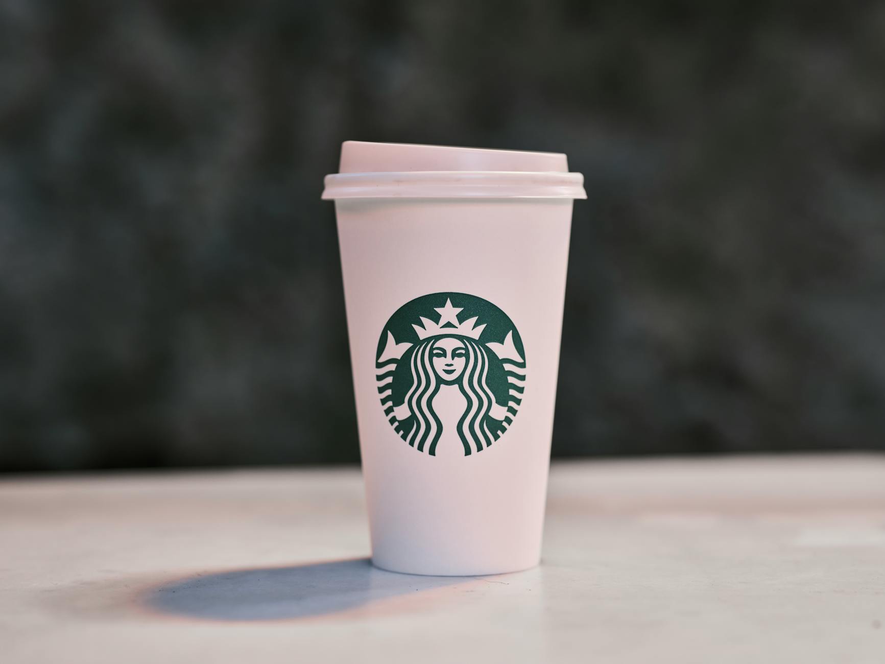 A disposable coffee cup with a recognizable logo on a table, captured with shallow focus.