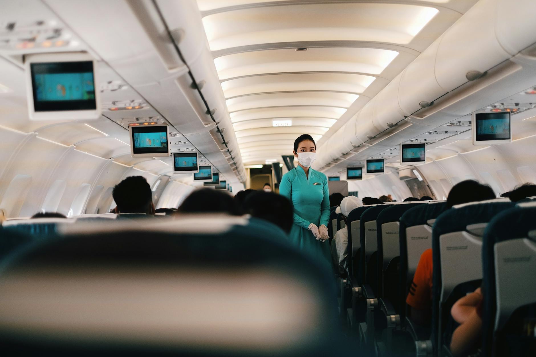 Flight attendant wearing a face mask attending to passengers in an airplane cabin.