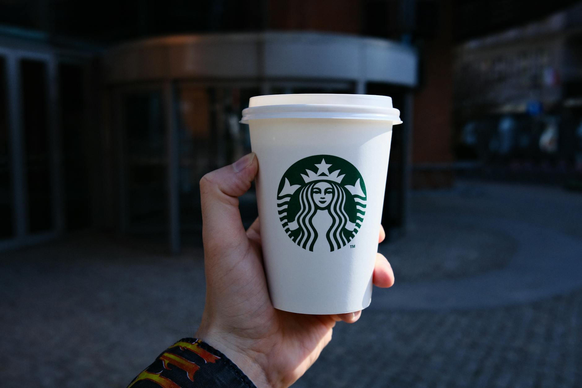 A hand holds a disposable coffee cup with a logo outdoors in Poznań, Poland.