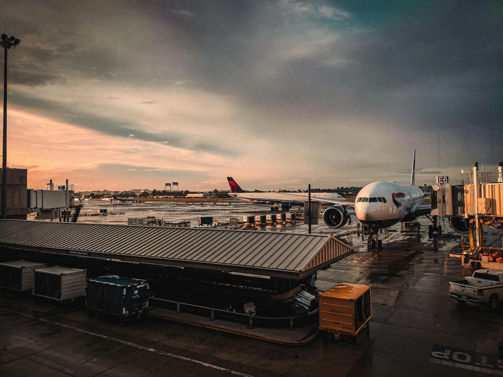 An airplane parked at an airport gate during sunset with reflections on wet tarmac.