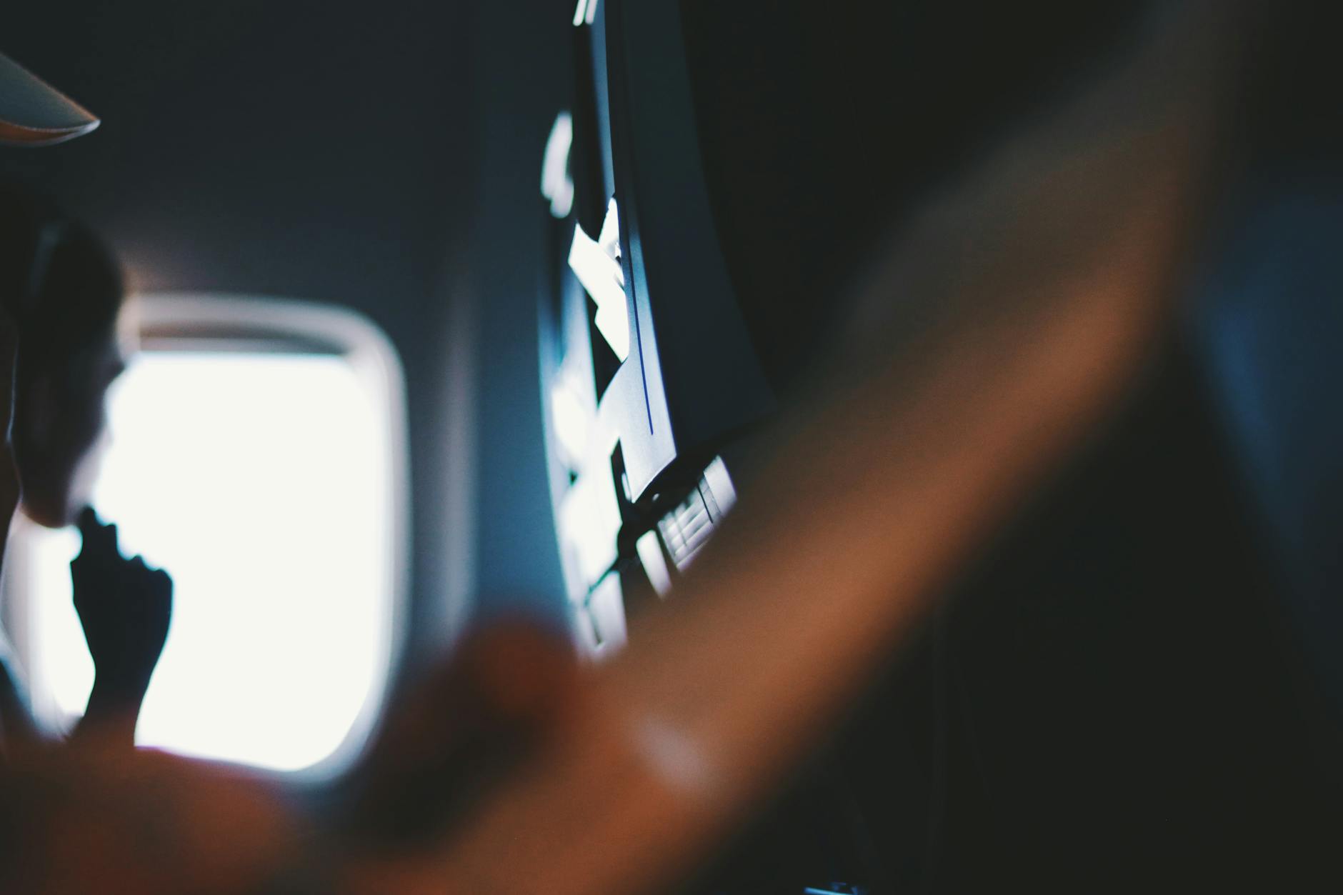 Close-up view of airplane window and entertainment screen with blurred foreground and person in the cabin.