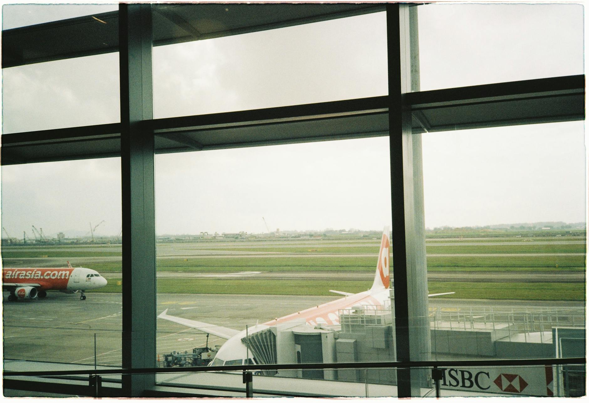 View of an AirAsia airplane parked at a terminal through large airport windows.