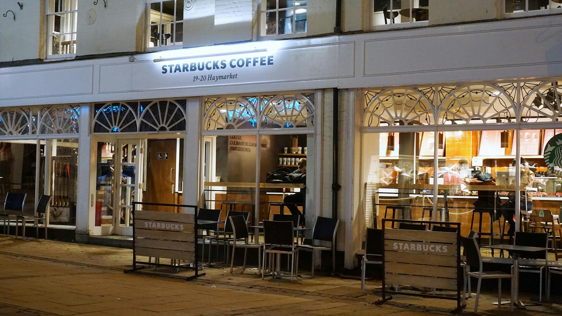 A cozy Starbucks café in Norwich with inviting exterior lights and seating at night.