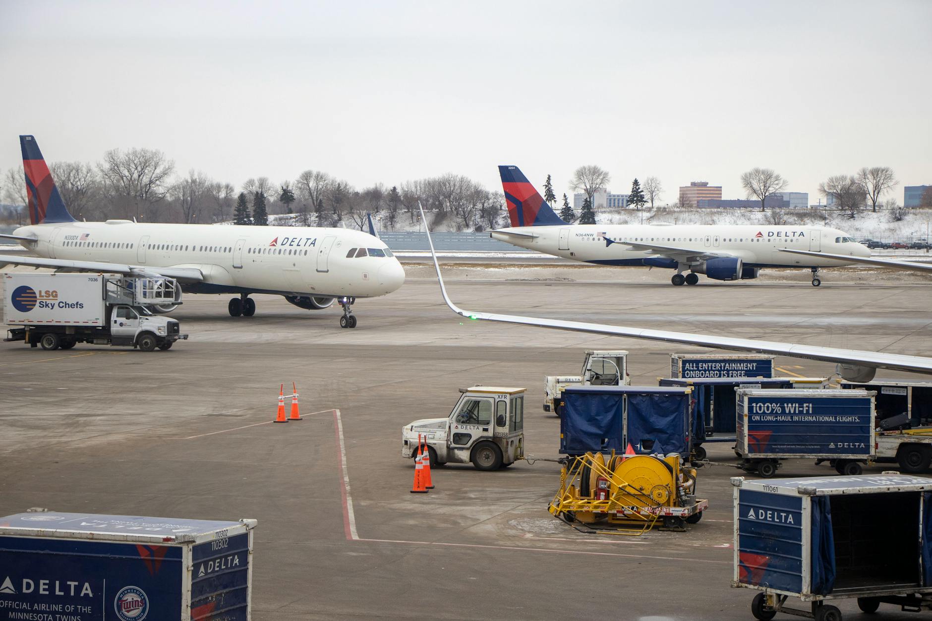 Delta airplanes on the snowy tarmac surrounded by service vehicles at a busy airport.